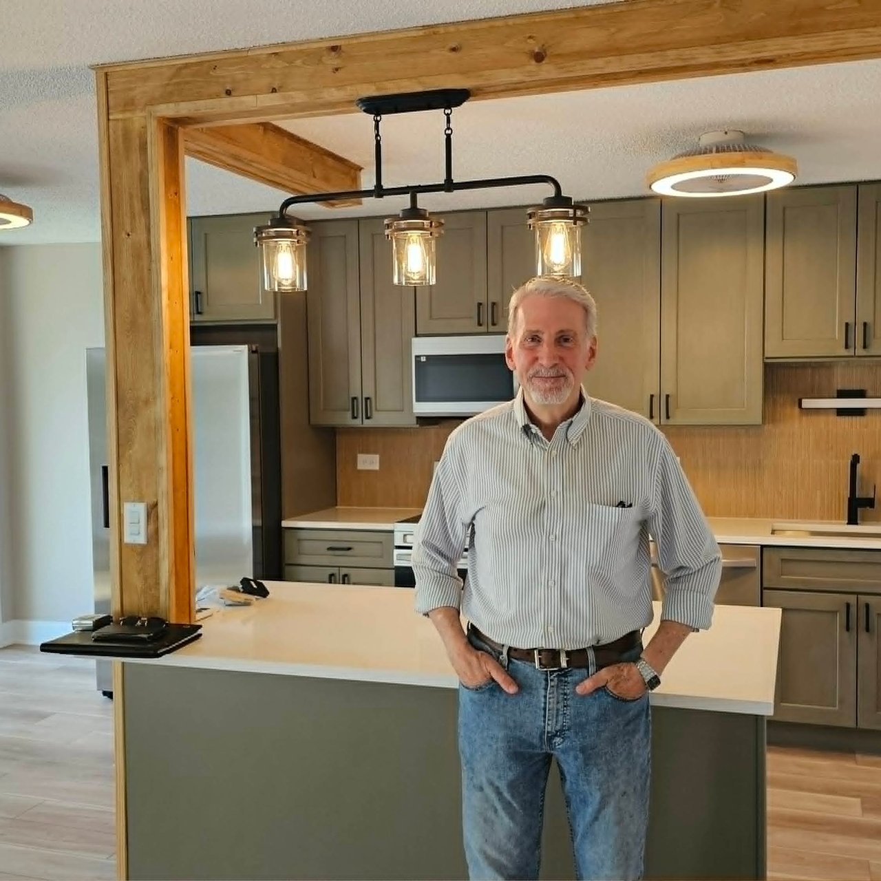 Older man standing in a renovated kitchen with gray cabinets and pendant lights.