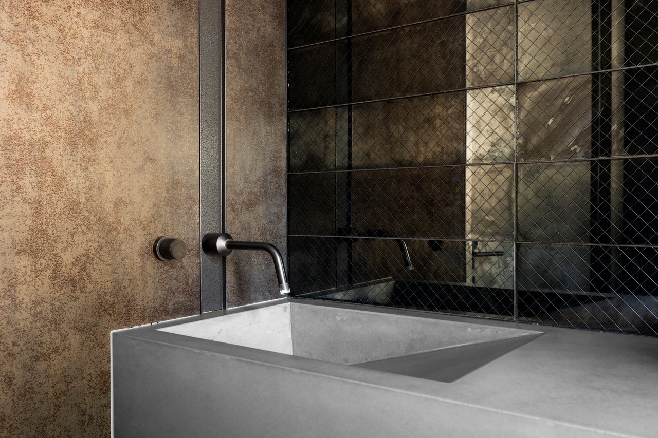 Minimalist bathroom sink with concrete vanity, wall-mounted faucet, and industrial reflective tile backsplash