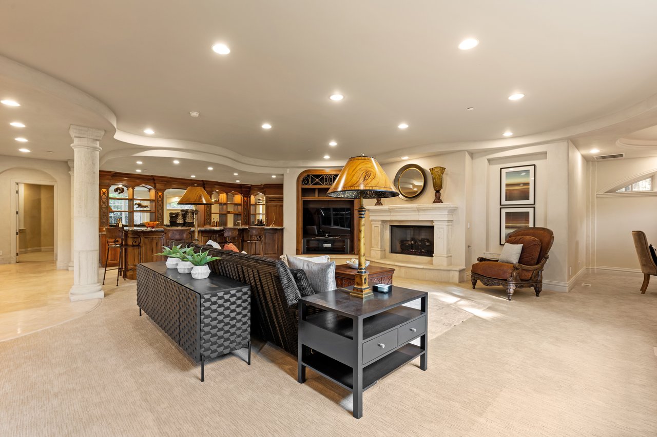 Living room with a stone fireplace, built-in bar cabinetry, and a sculpted curved ceiling.