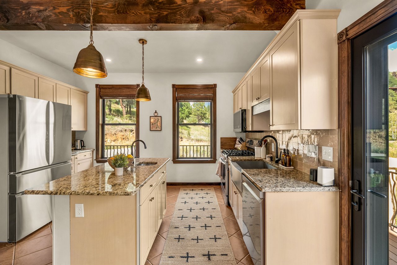 Kitchen with cream cabinets, granite island, stainless steel appliances, and windows overlooking trees.