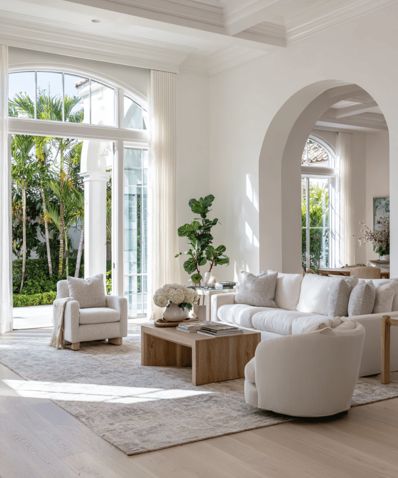 Bright living room with white seating, high arched windows, and tropical greenery outside.