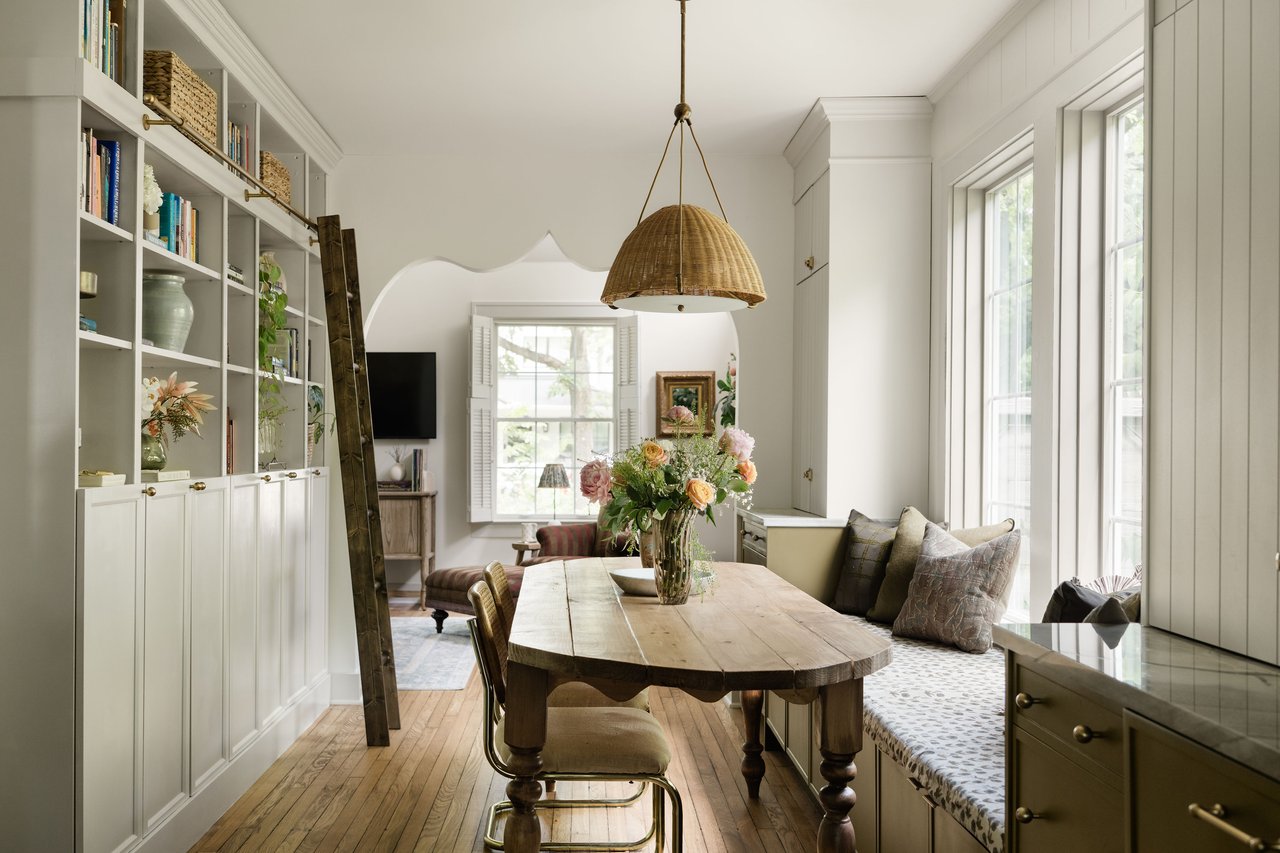 Dining room with a rustic wooden table, built-in bookshelves, and a window-seat bench.