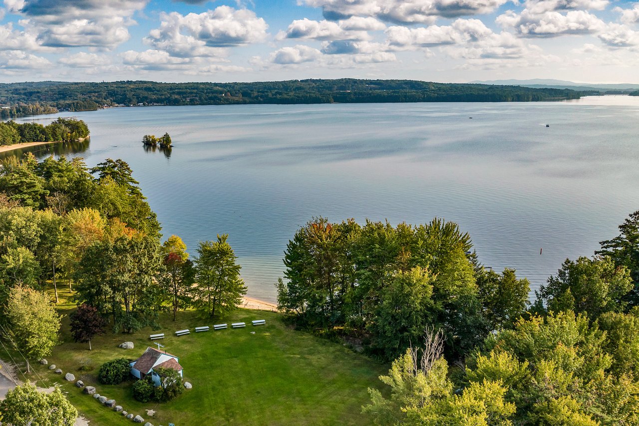 Aerial view of a broad lake with wooded shores, a small island, and a grassy waterfront area.