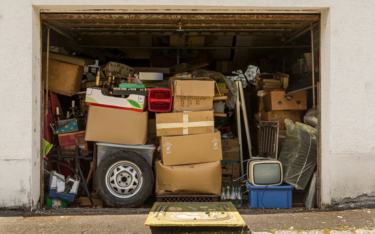 Cluttered garage packed with boxes, a spare wheel, and an old television.