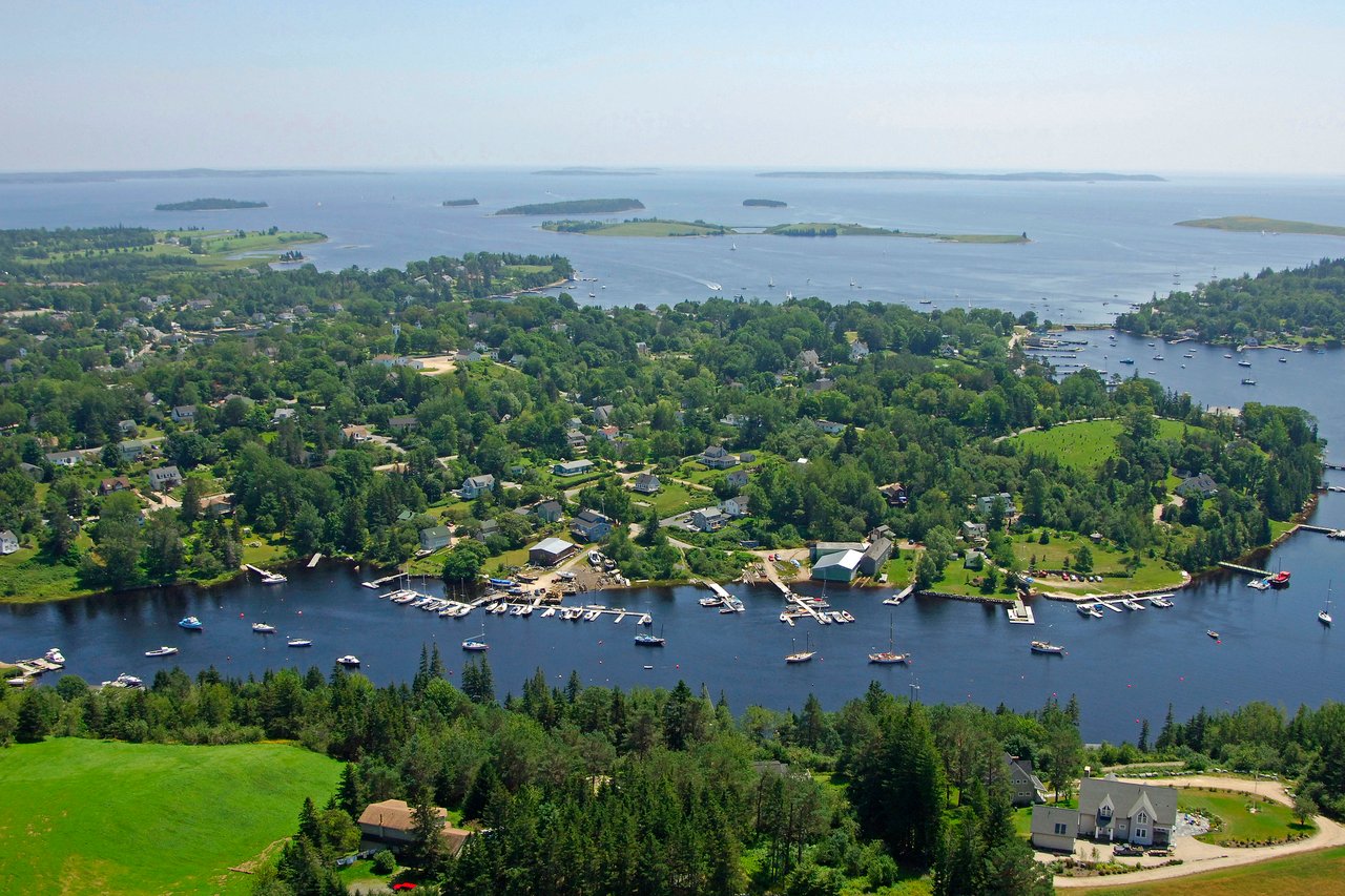 Aerial view of a wooded coastal neighborhood with waterfront homes, docks, and boats.