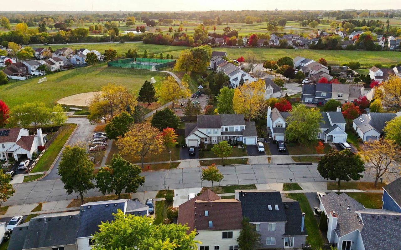 Aerial view of suburban homes beside a park with sports courts and colorful autumn trees.