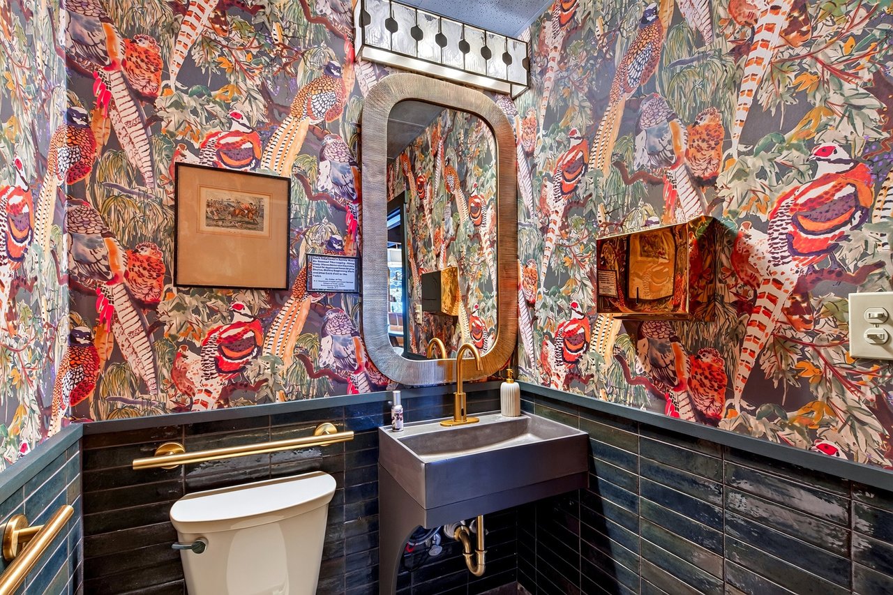 Restaurant bathroom with vivid bird-print wallpaper, dark tile, a square sink, and a large mirror.