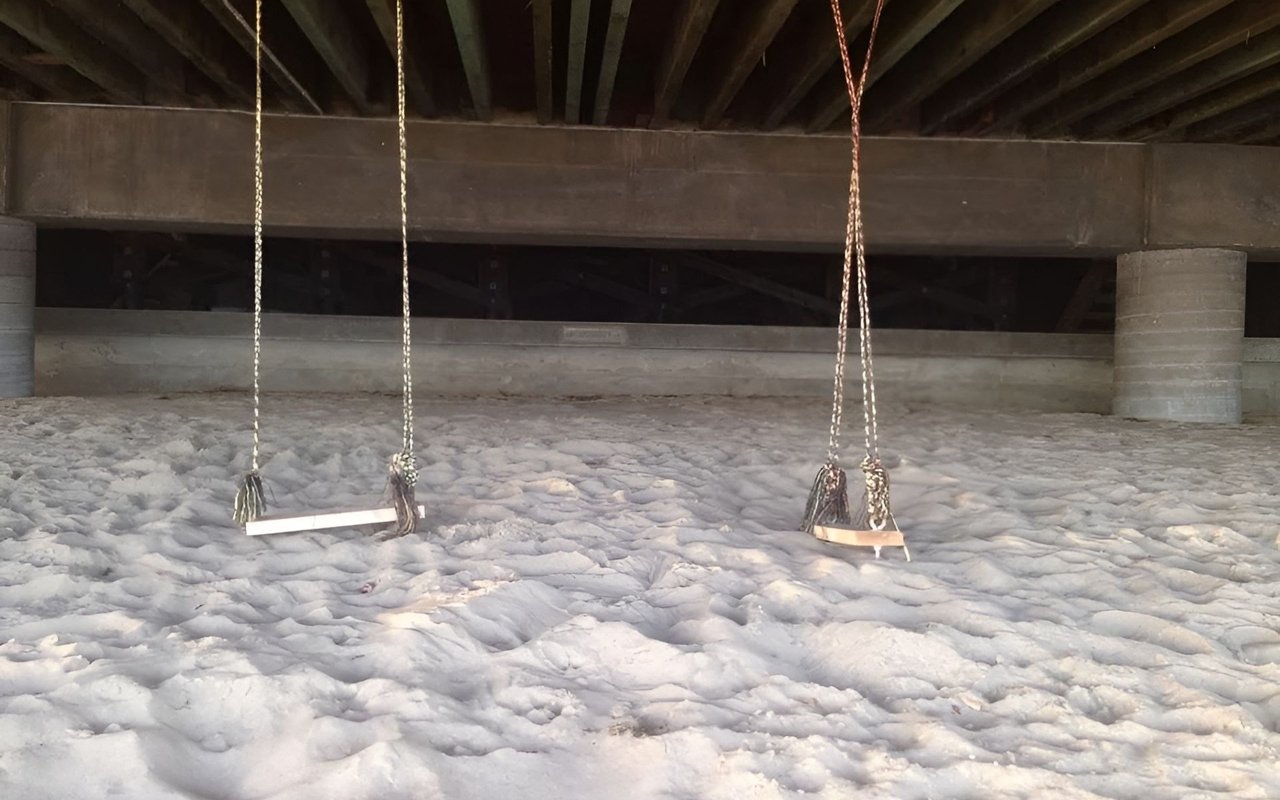 Two rope swings hang above pale sand beneath a low concrete structure.