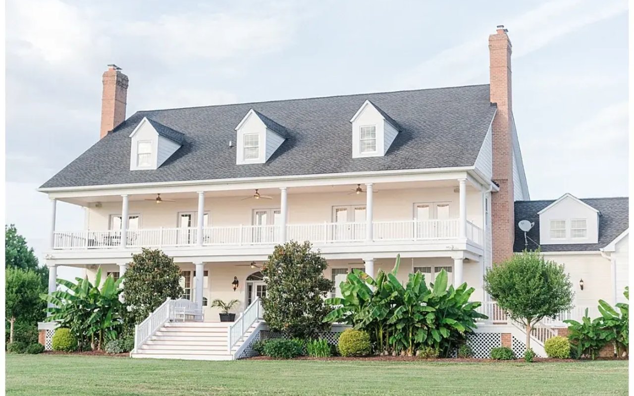 White house with two-story porches, three roof dormers, and tall brick chimneys.