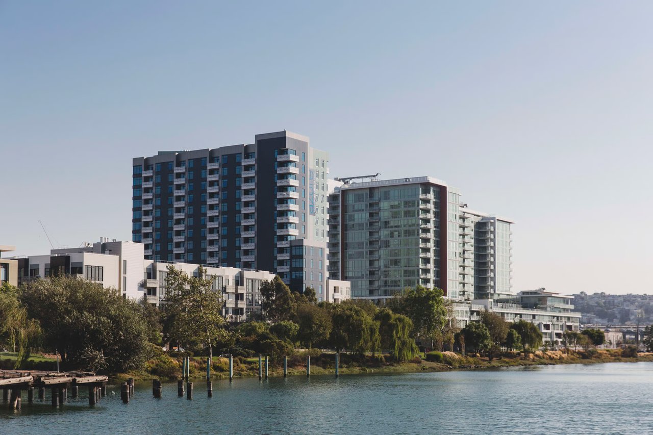 Modern apartment buildings along the waterfront, with balconies, landscaped grounds, and a dock.