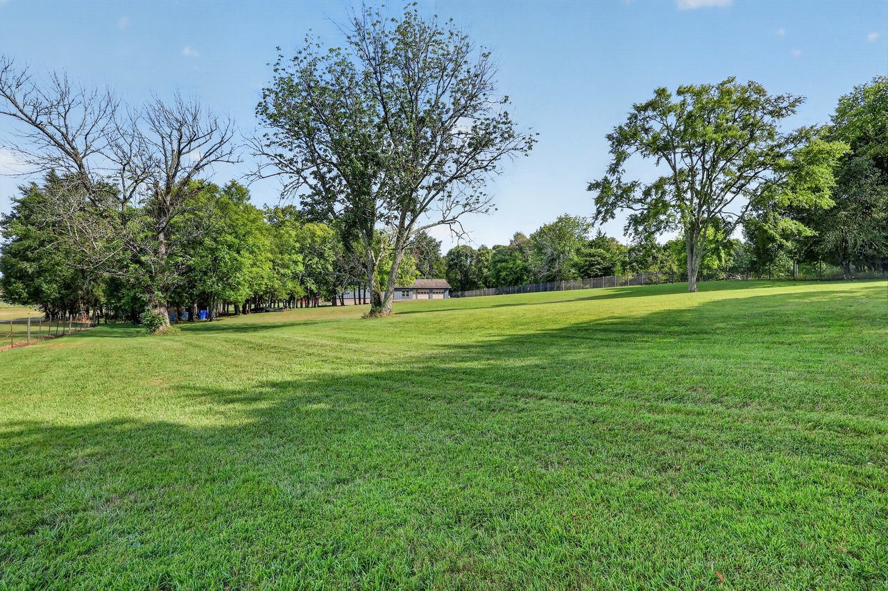 Grassy property with mature trees, a small outbuilding, and fencing along the back.