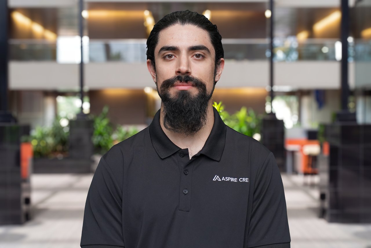 Rick Martinez in a black Aspire CRE polo in a modern office lobby.