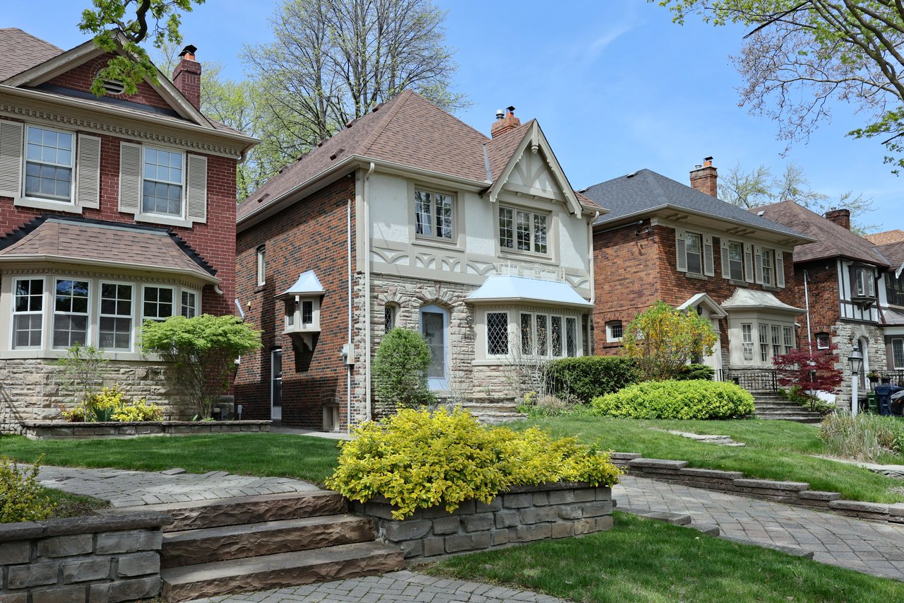 Toronto residential streetscape with brick and stone homes, landscaped front yards, and mature trees.