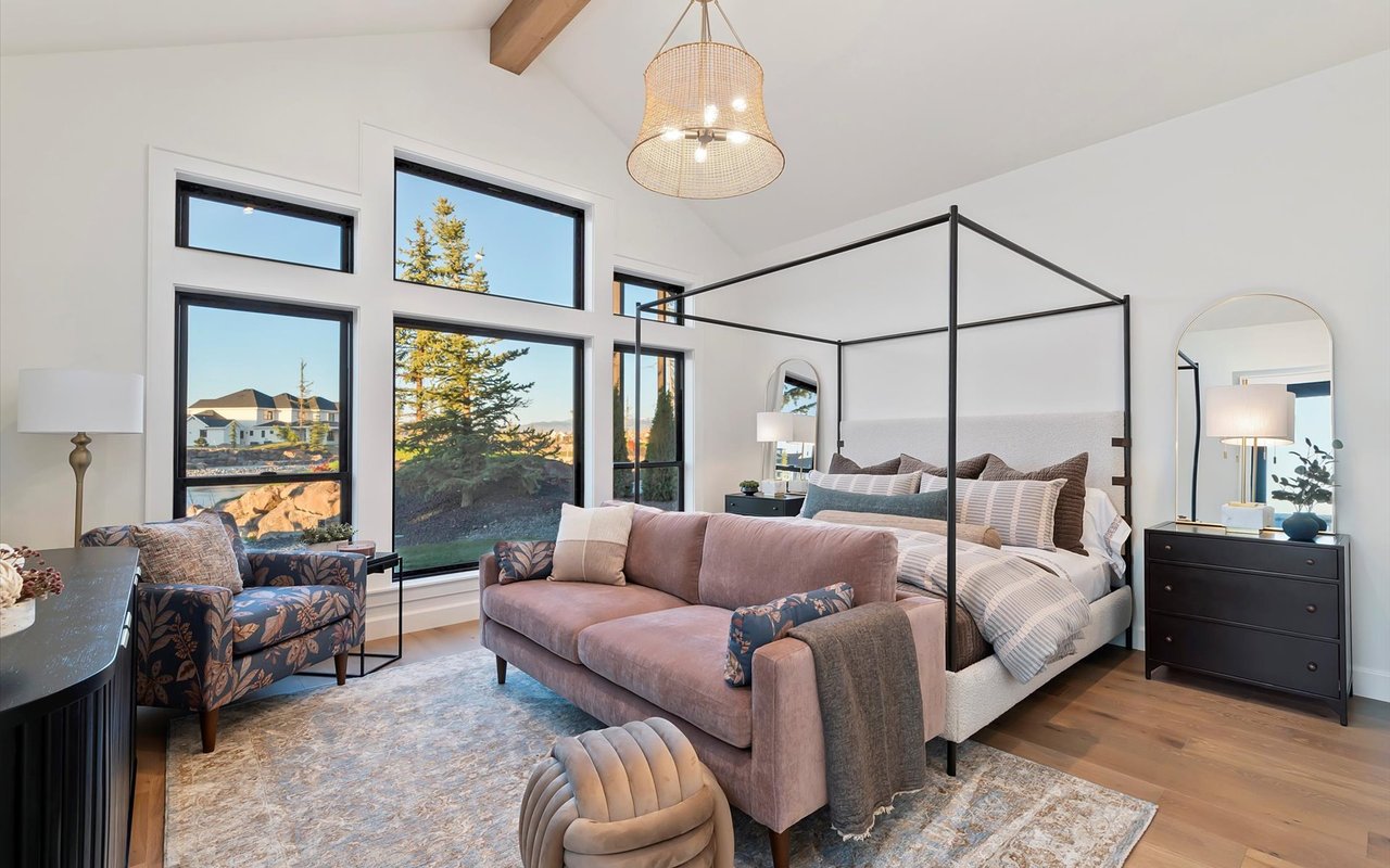 The main-level primary bedroom with vaulted ceiling, wood beam and three oversized floor-to-ceiling windows overlooking the lake