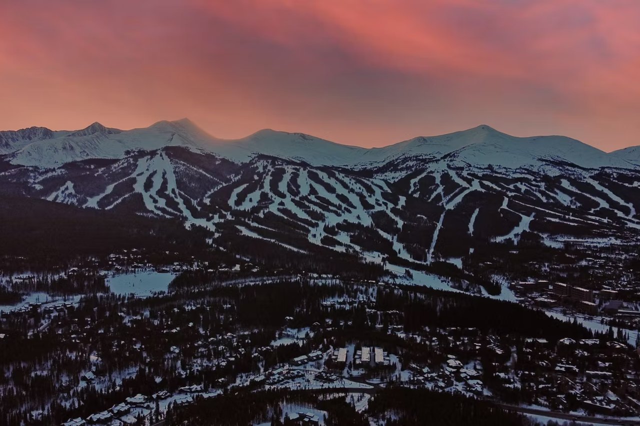 Snowy ski runs and a mountain town beneath a pink sunset sky.