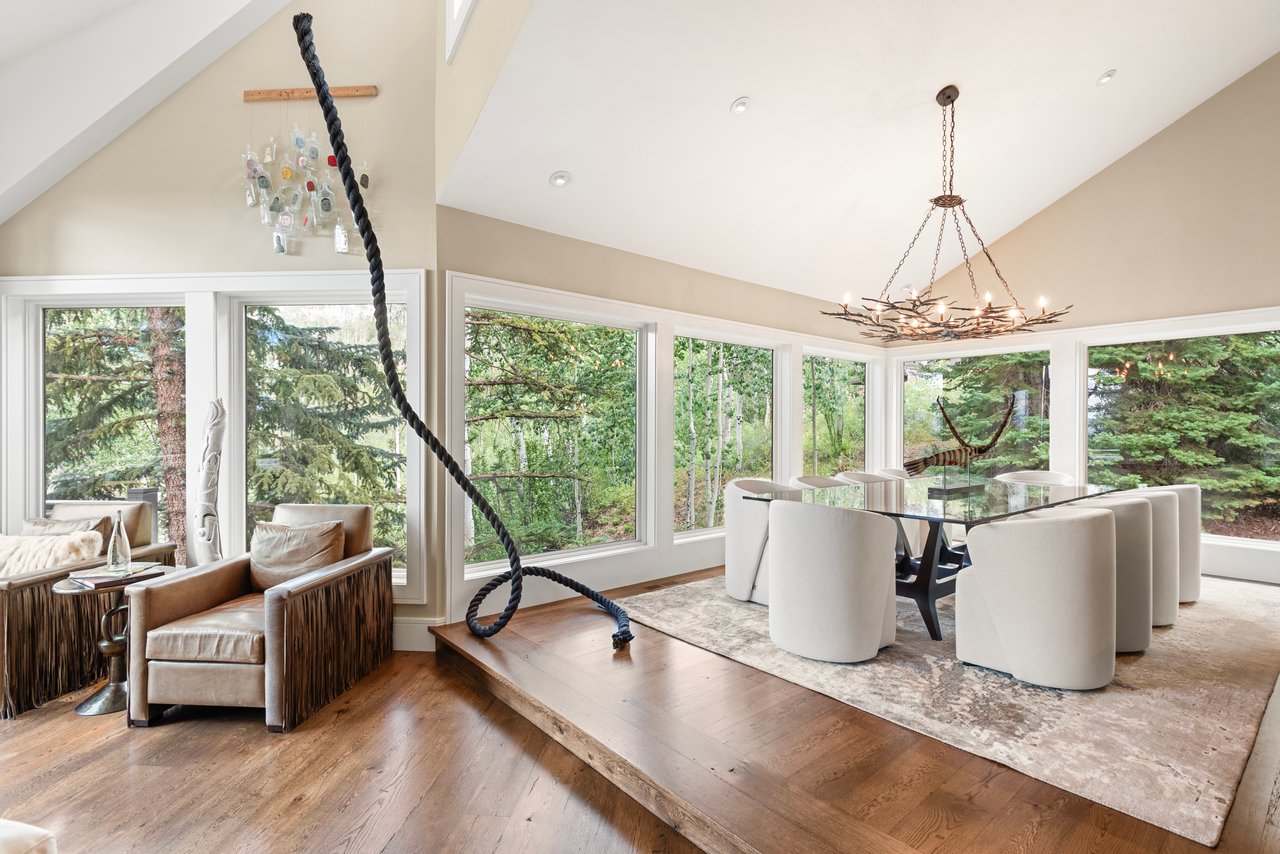 Dining room with a branch chandelier, forest-facing windows, and an adjoining sitting area.
