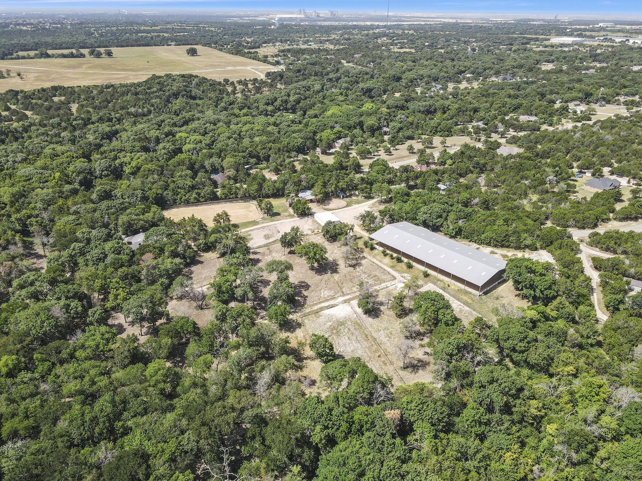Aerial view of wooded acreage with open fields, scattered homes, and a large barn.
