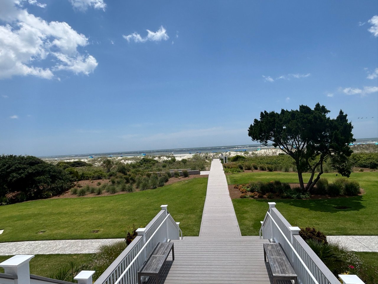 Wooden beach walkway crossing a green lawn and dunes toward the ocean.