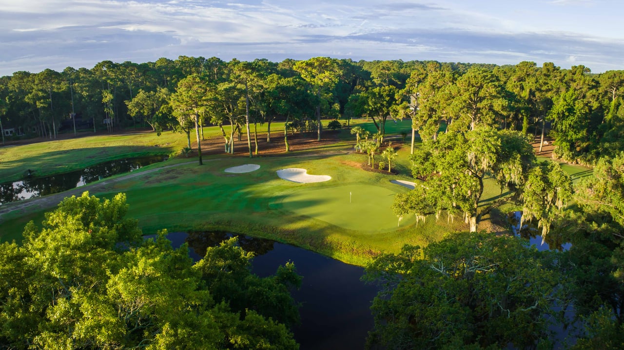 Aerial view of a golf green with sand bunkers, ponds, and mature trees.