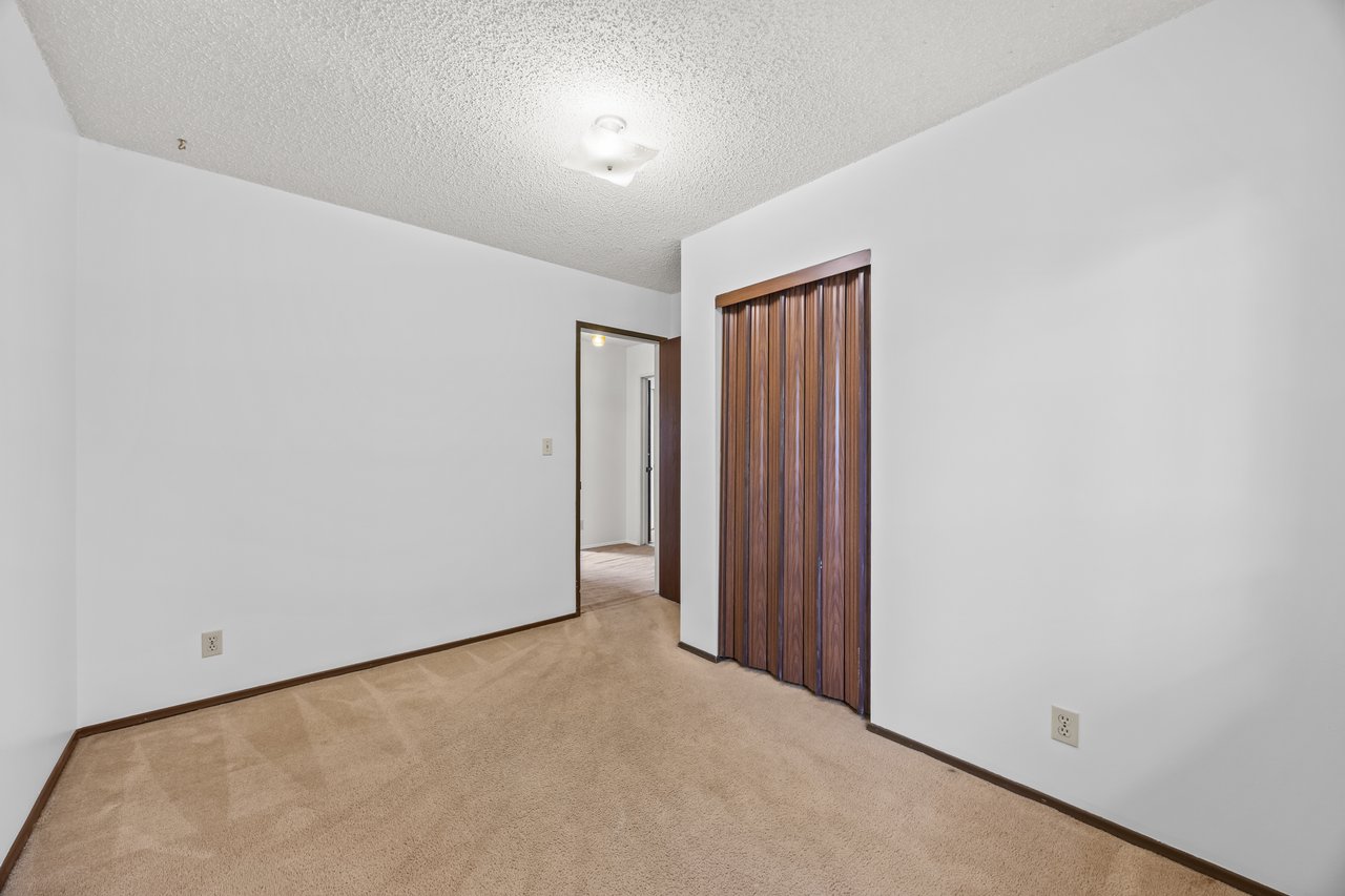 Empty carpeted bedroom with wood-paneled closet doors and an open doorway.