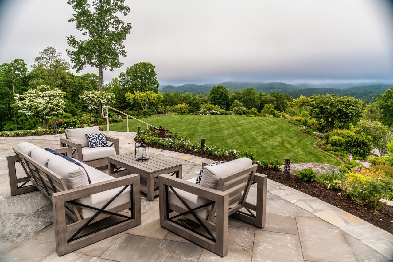 Stone patio with outdoor seating overlooking a lawn, gardens, and mountains at the Trillium clubhouse near Cashiers, NC