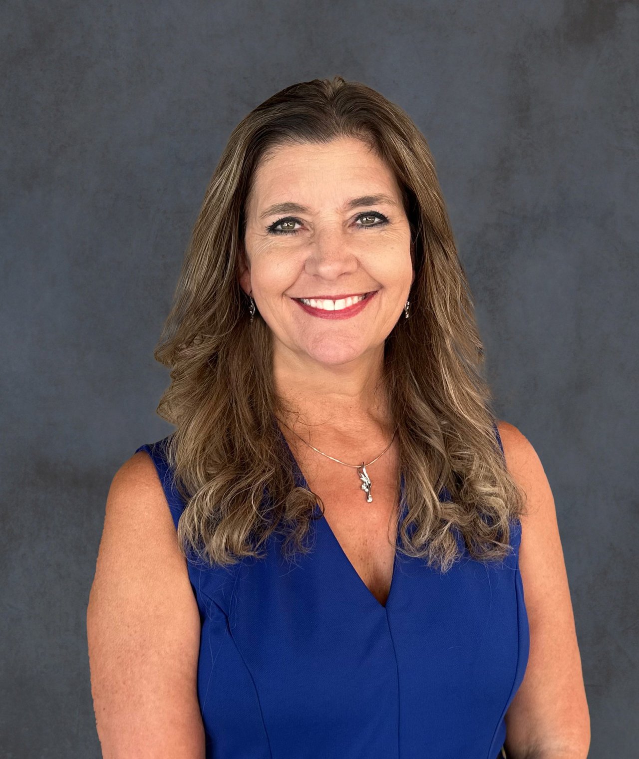 Cherie Smith smiling in a blue sleeveless top and pendant necklace.