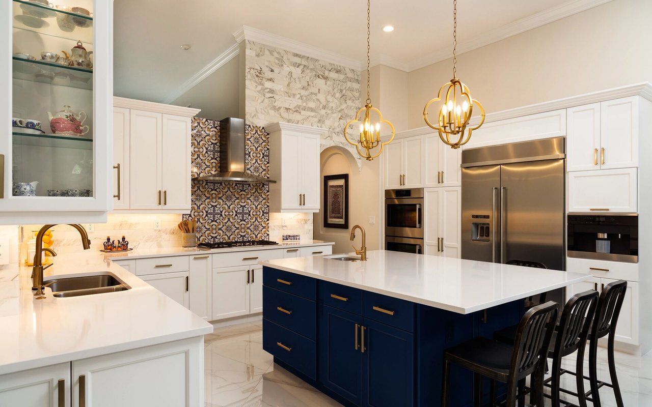 Upscale kitchen with a navy island, patterned range backsplash, and gold pendant lights.