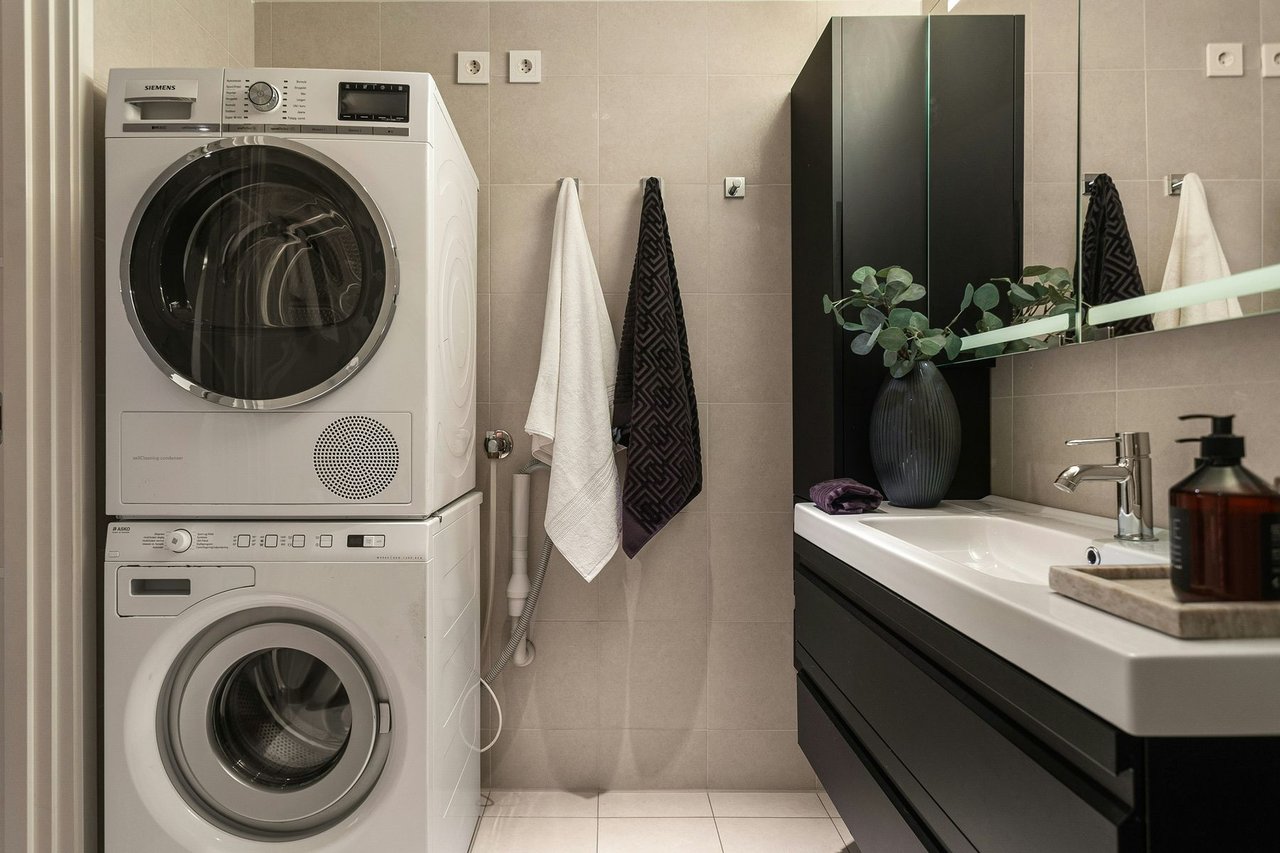 Stacked washer and dryer in a modern NYC apartment bathroom with tiled walls, vanity and compact in-unit laundry setup.