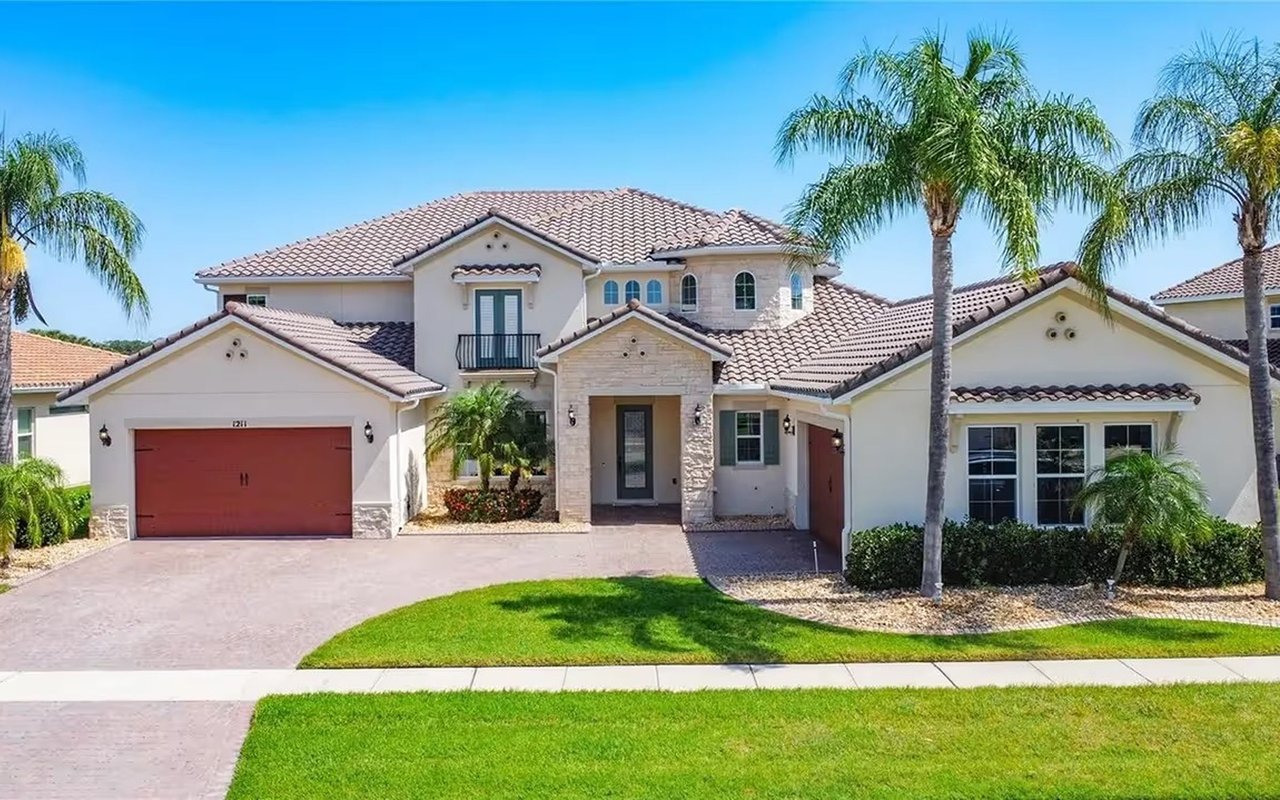 Two-story stucco home with a tiled roof, red-brown garage doors, and palm trees.