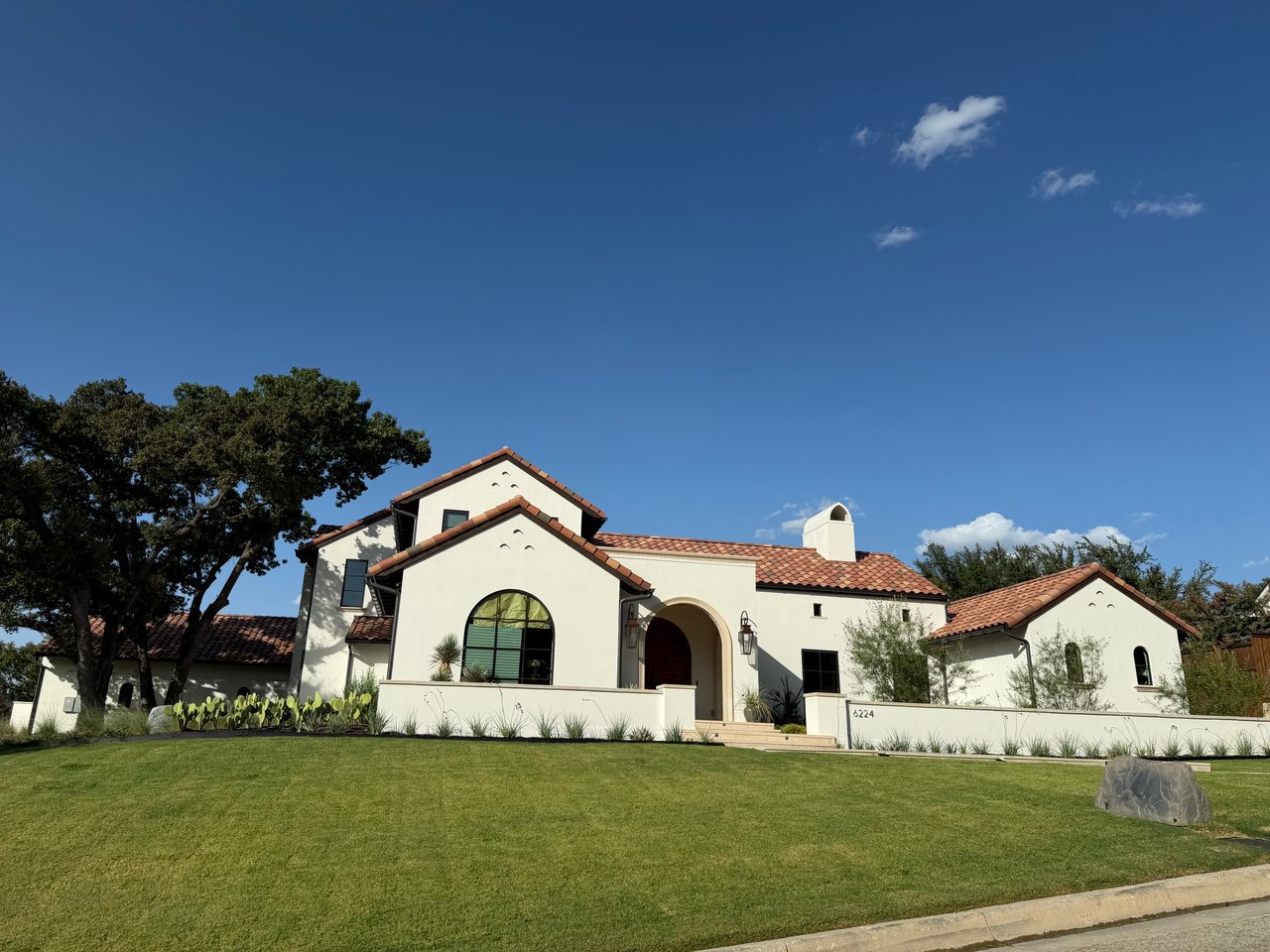Cream stucco house with terracotta tile roofs, an arched entryway, and a broad lawn.