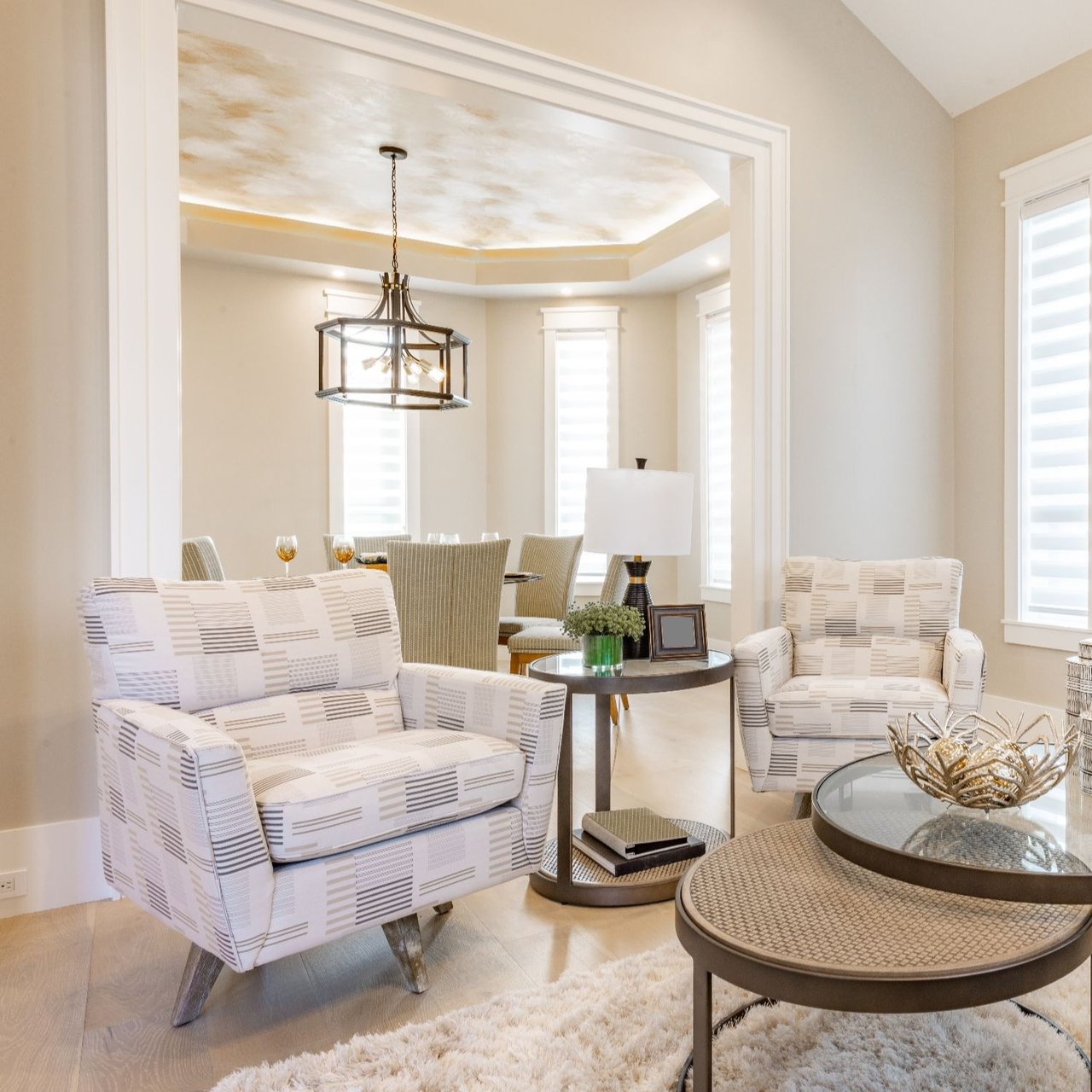 Bright living room with patterned armchairs, round coffee tables, and a dining area beyond.