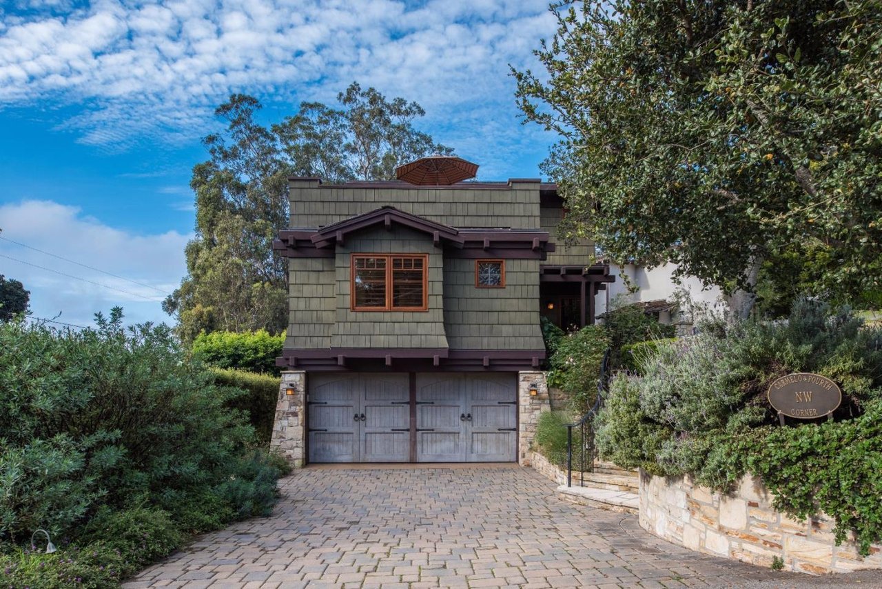 Gray shingle-sided home with double garage, stone-paver driveway, and a Carmelo & Fourth corner sign.