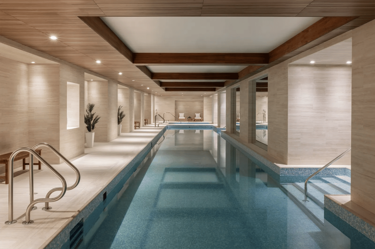 Indoor pool with blue mosaic tile, pale stone walls, and dark wood ceiling beams.