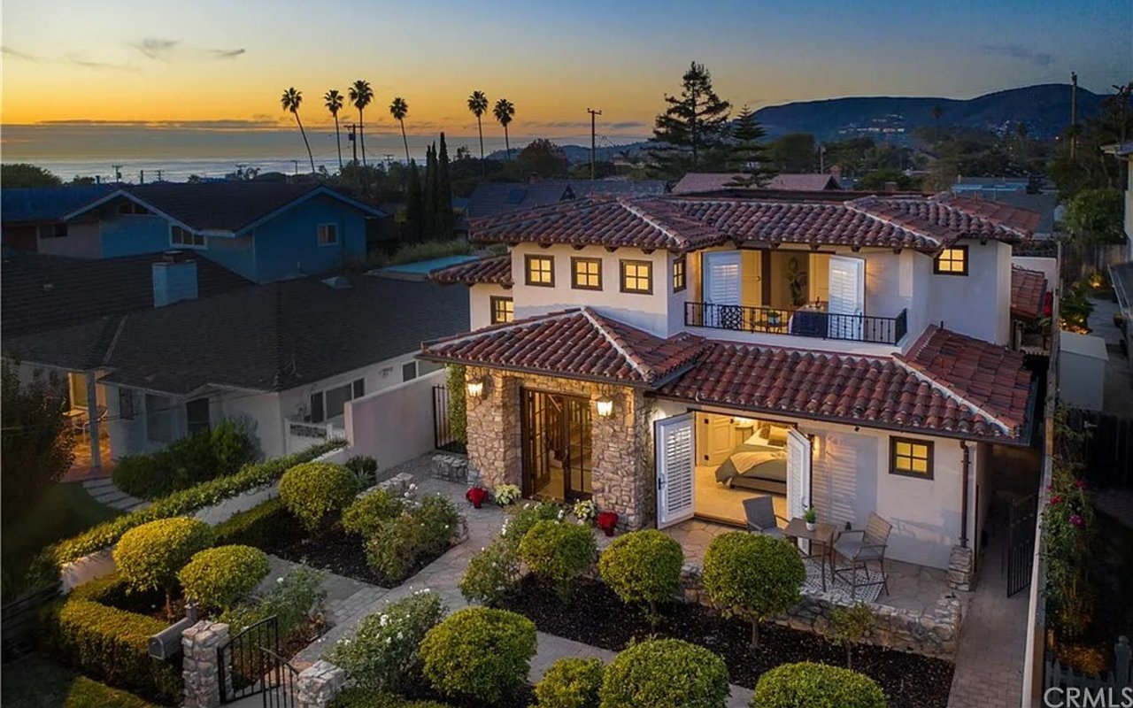 Aerial view of a Spanish-style home with landscaped courtyard and ocean sunset beyond.