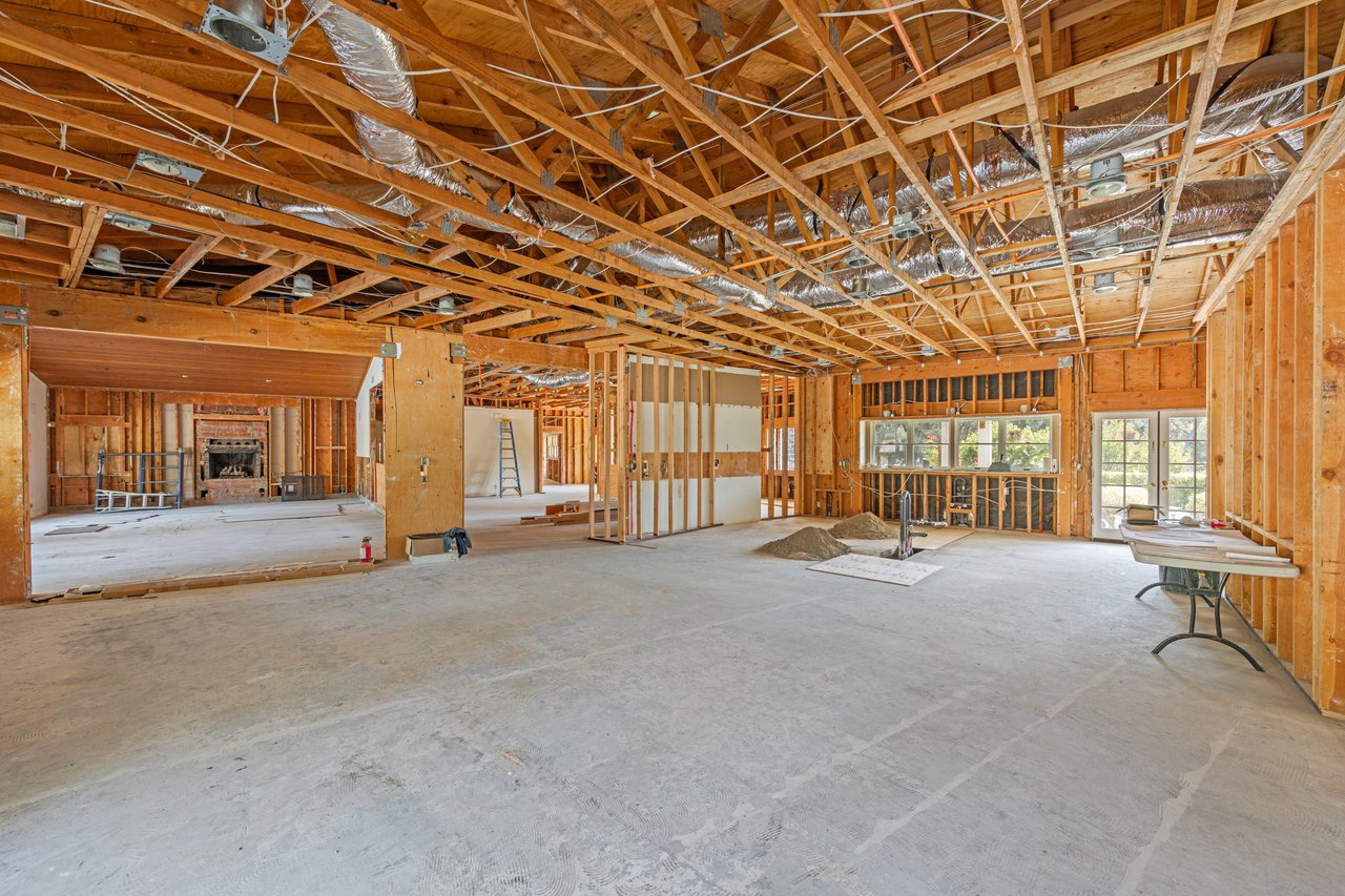 Unfinished open interior with exposed ceiling framing, a brick fireplace, and concrete floors.