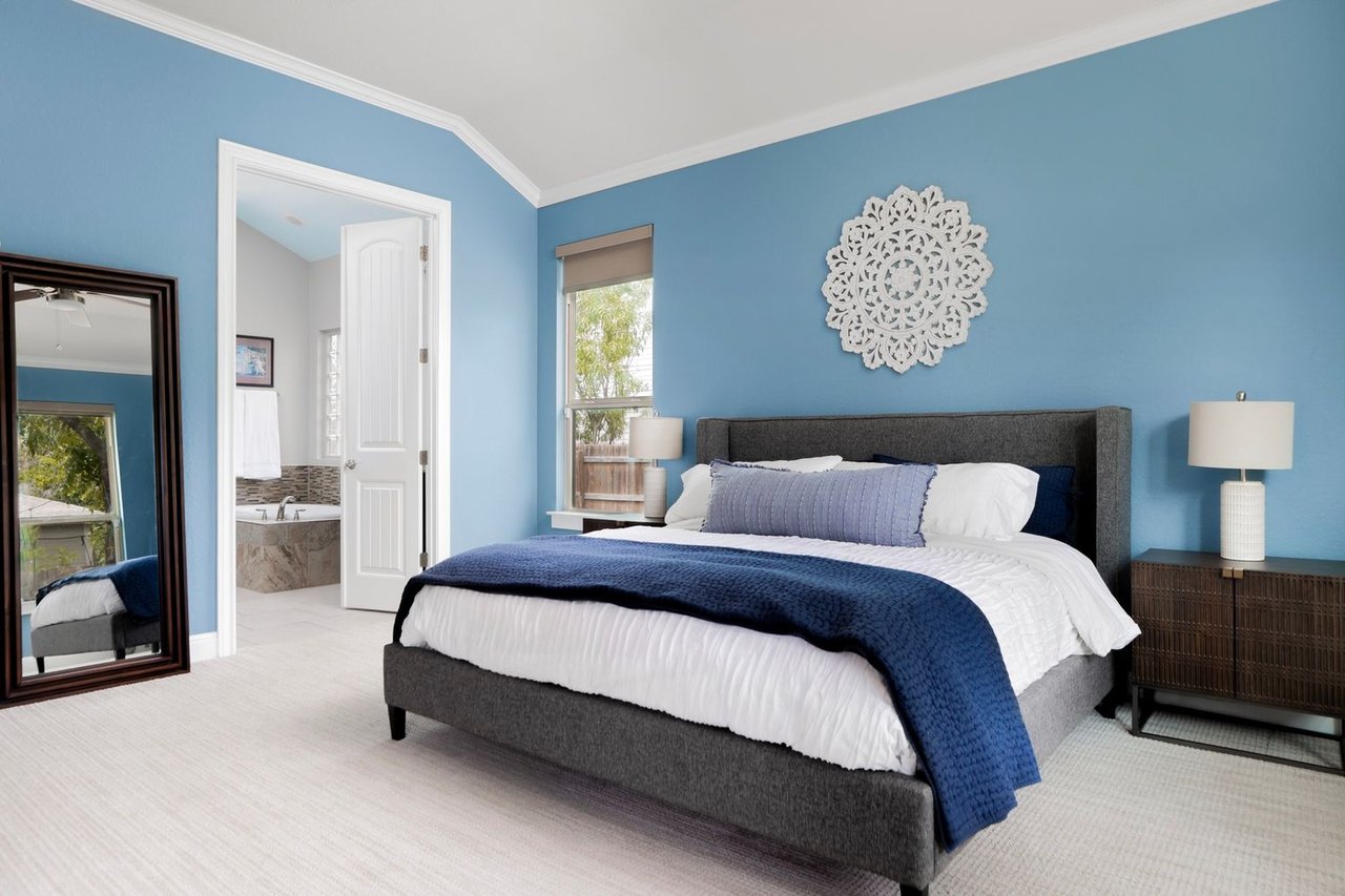 Furnished bedroom with blue walls, a gray bed, navy bedding, and an open doorway to the bathroom.