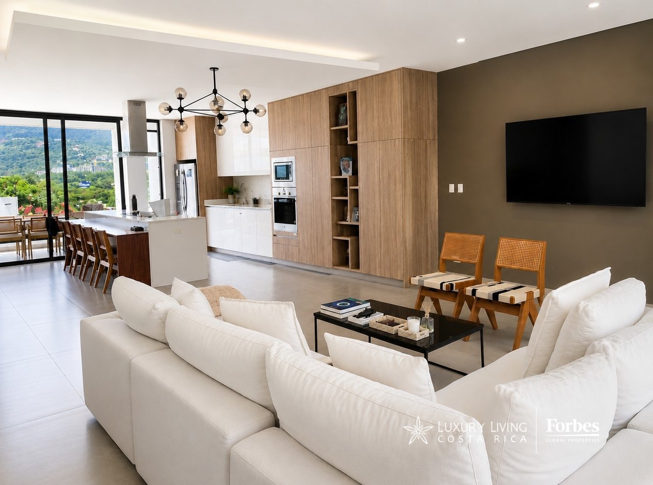 Open-plan kitchen and living room with white sofas, wood cabinetry, and mountain views through large windows.