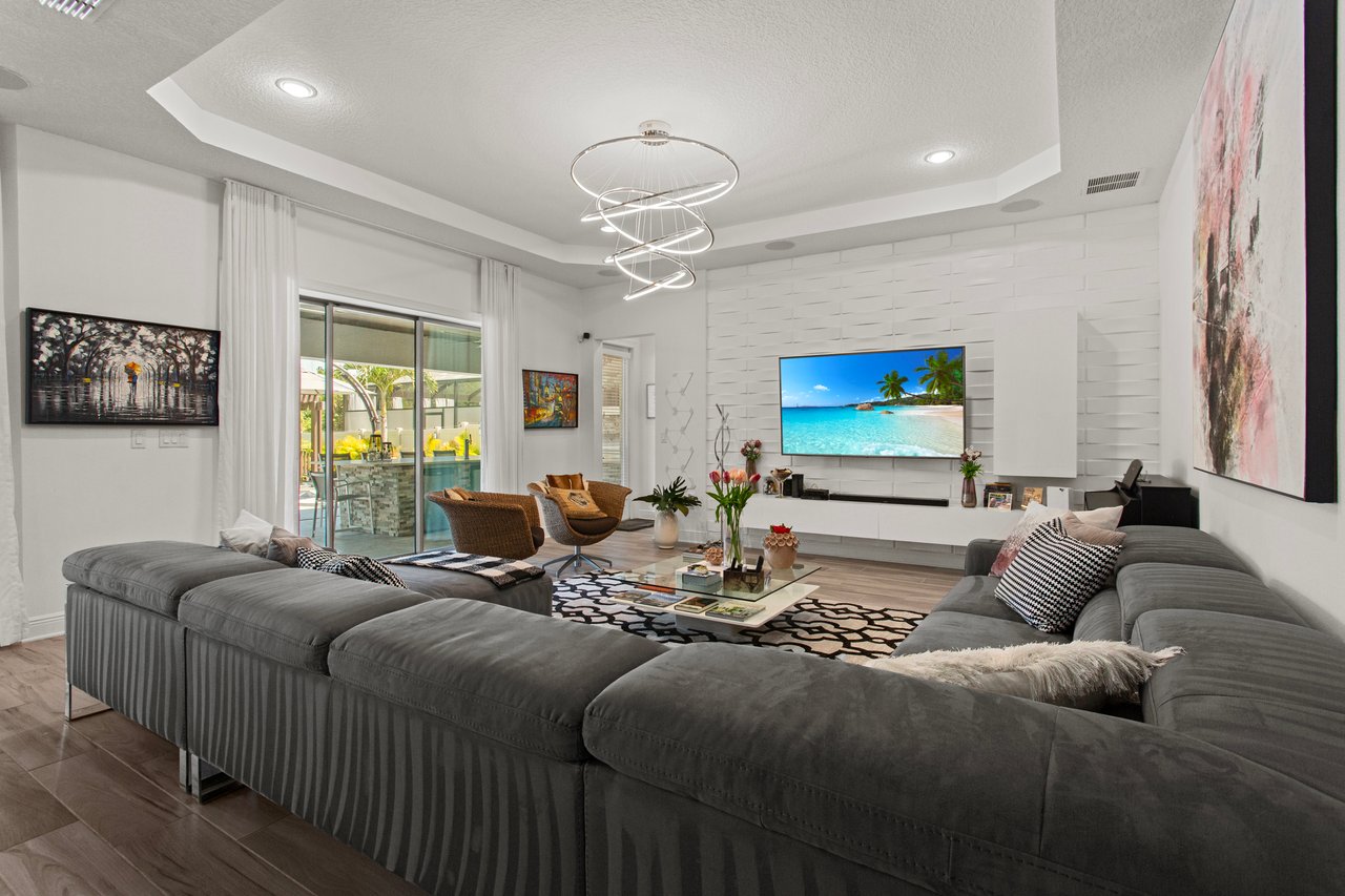 Living room with a large gray sectional, sculptural chandelier, and sliding glass doors to a patio.