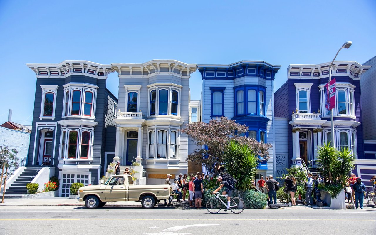Colorful Victorian houses with ornate trim and bay windows line a sunny street.