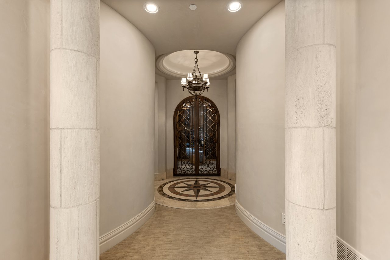 Curved entry hallway with stone columns, a compass-rose floor medallion, and an ornate arched iron door.