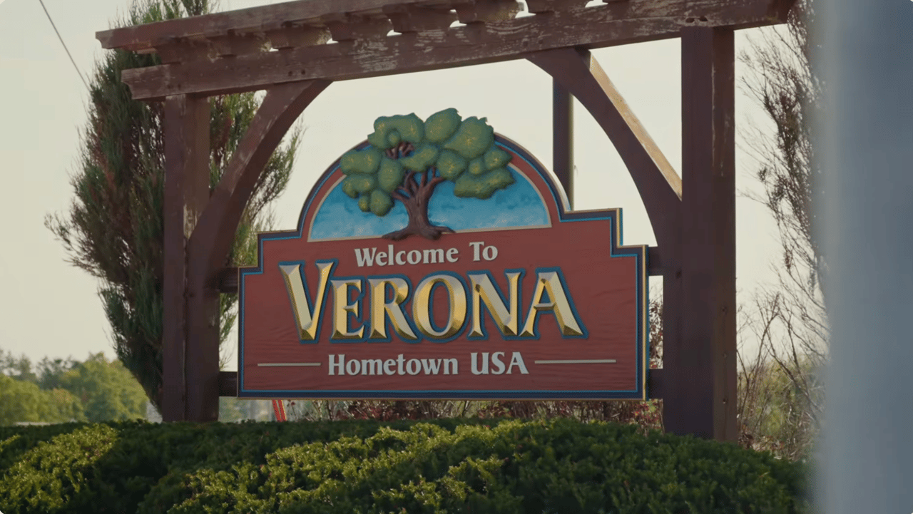 The official wooden Welcome to Verona, Hometown USA community sign featuring a tree design, surrounded by green landscaping in Verona, Wisconsin.