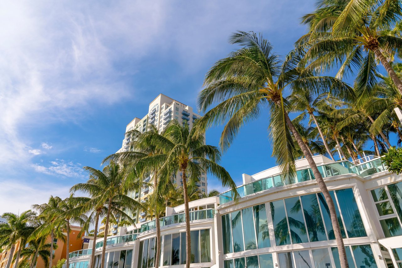 Modern condominium buildings with glass balconies and tall palm trees beneath a blue sky.