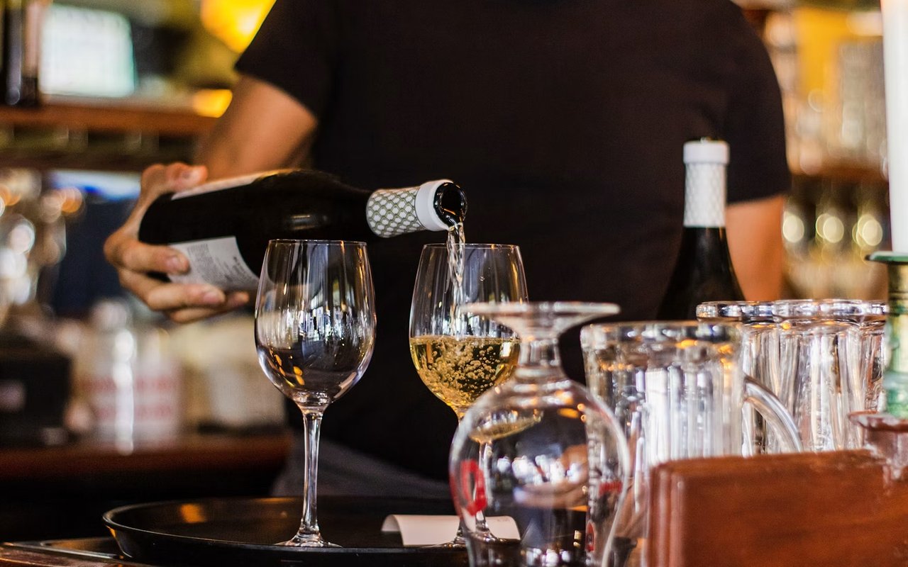 Bartender pours sparkling wine into a glass at a warmly lit bar.