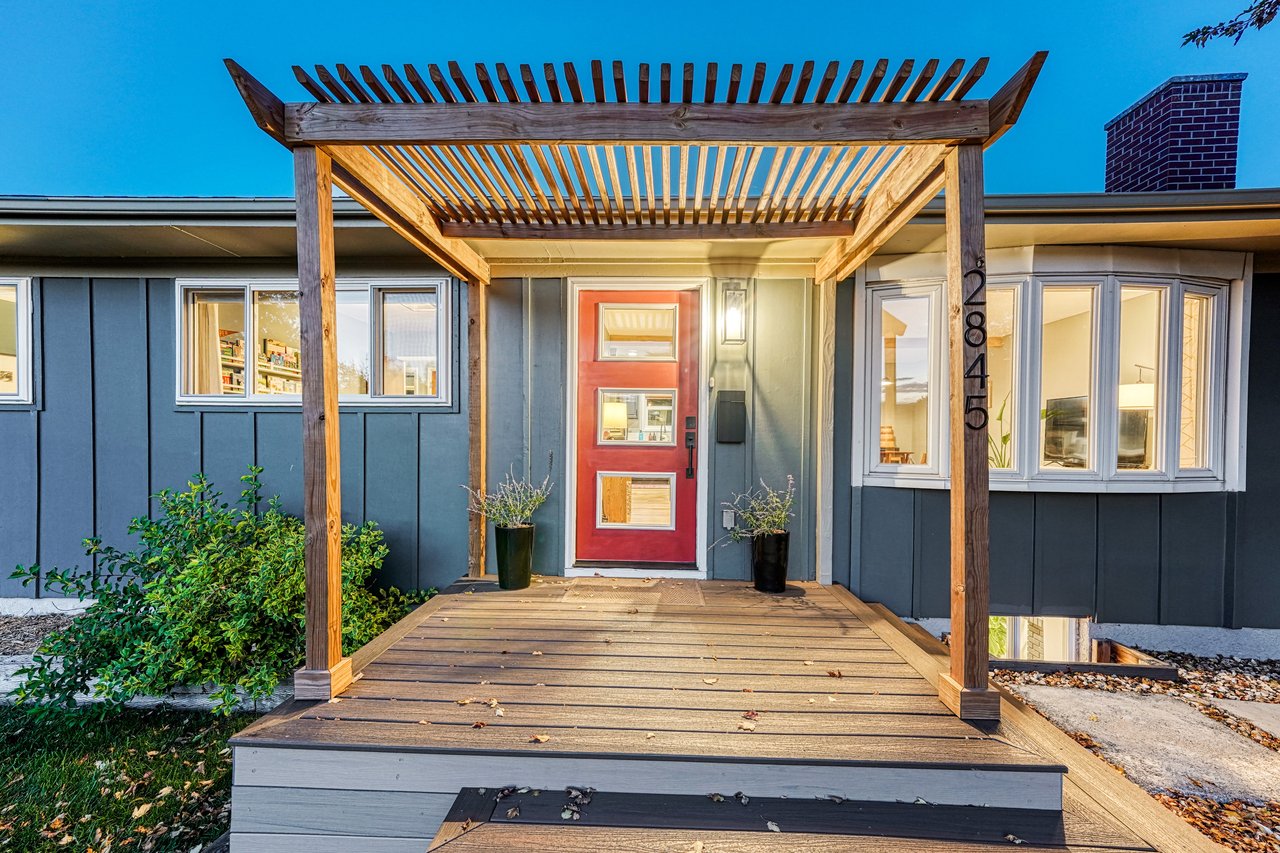 Front entry at dusk with a wood pergola over the porch and a red modern front door