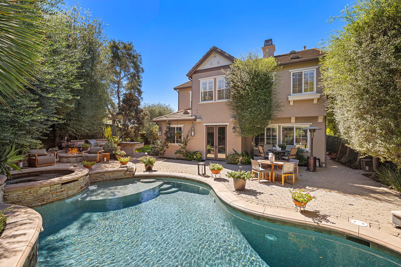 Backyard pool and raised spa beside a two-story home, with a furnished patio and fire pit.