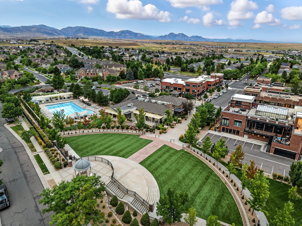 Aerial view of the Five Parks neighborhood in Arvada, Denver, CO featuring a landscaped community park, clubhouse, outdoor pool, and mountain views in the background.