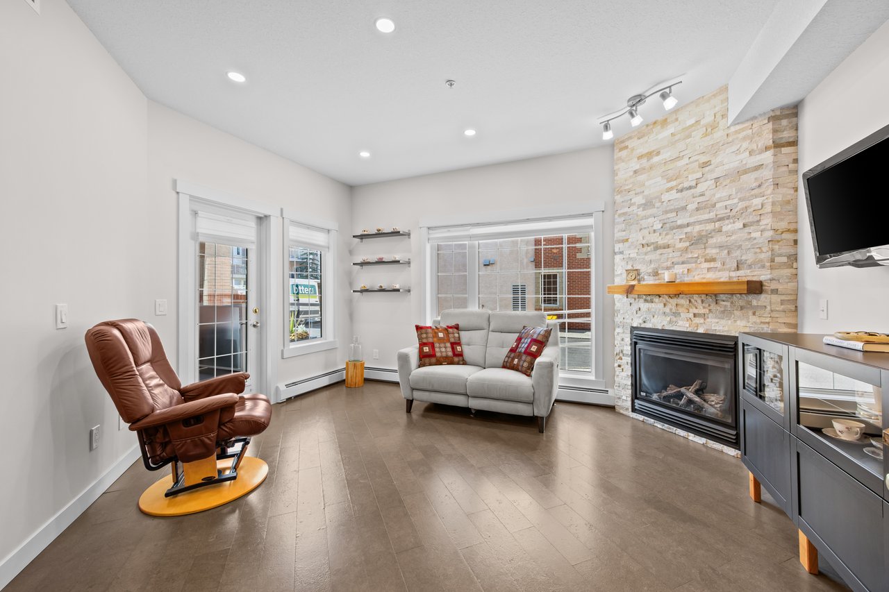 Living room with a stone fireplace, gray loveseat, and brown recliner beside large windows.