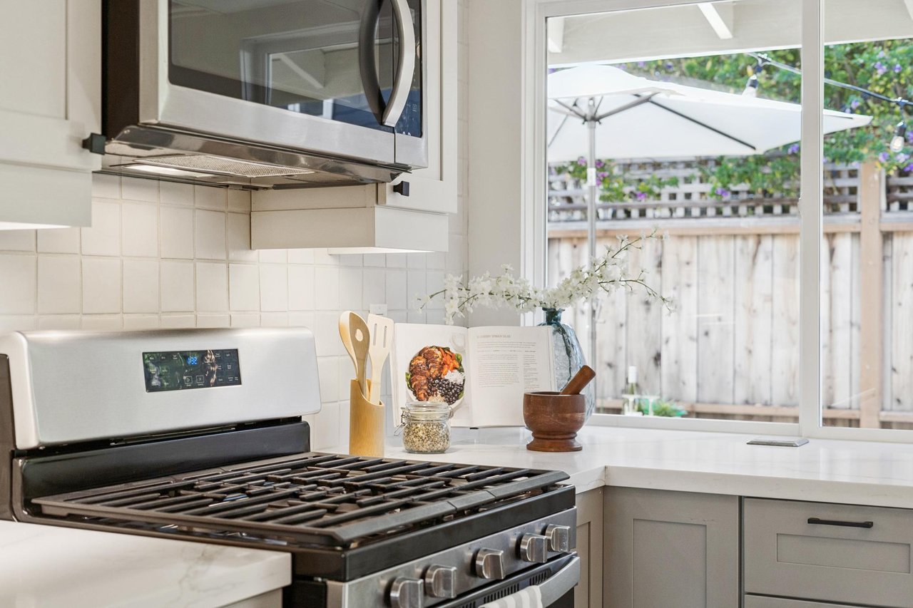 Bright kitchen with stainless-steel range and a window overlooking a fenced patio and white umbrella.