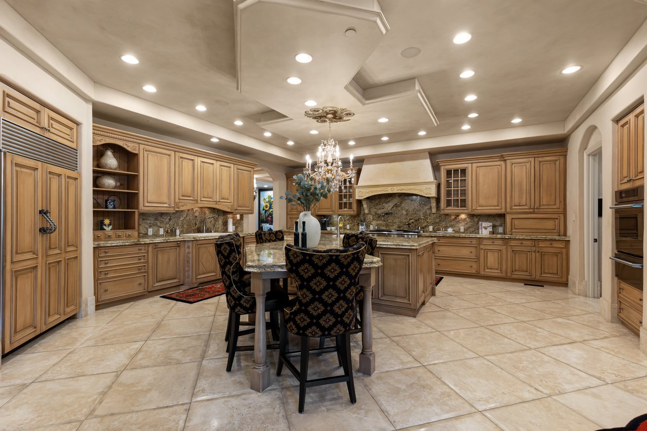 Luxury kitchen with warm wood cabinetry, a stone backsplash, and a central island with seating.