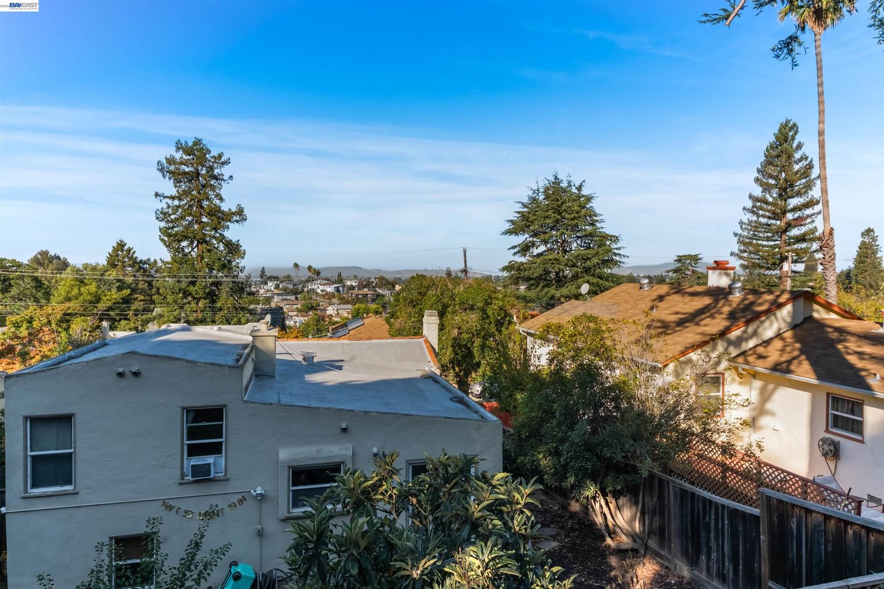 Backyard view over neighboring Oakland homes and rooftops, framed by trees.